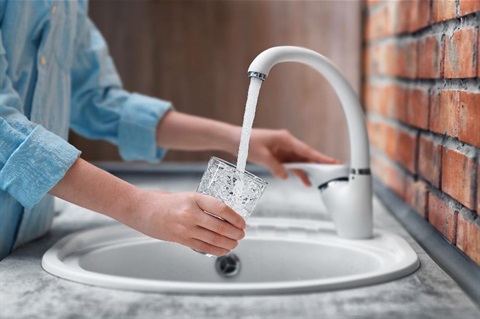 A woman using a tap to fill up a glass of water.