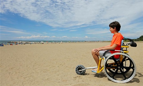 A boy in a wheelchair on a sandy beach.