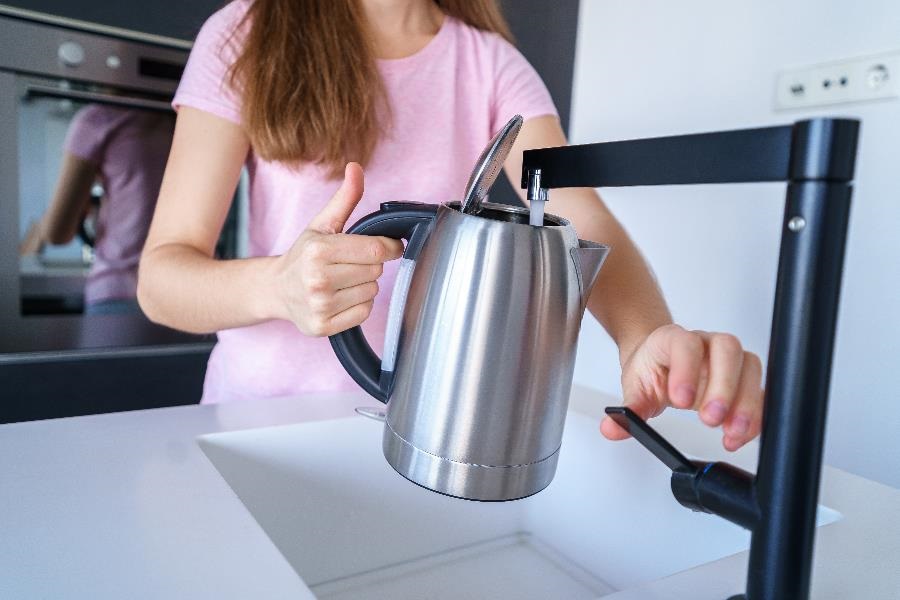 A woman fills a kettle with tap water.