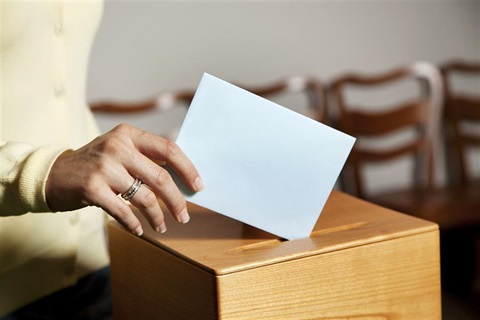 A woman puts her voting envelope into a wooden box.